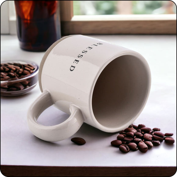 Blessed stoneware mug resting on its side with coffee beans spilling around it, perfect for coffee lovers