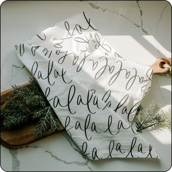 Festive Fa La La tea towel displayed flat on a decorated holiday table