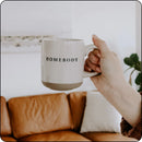Person holding Homebody stoneware mug with a leather couch in the background, ideal for relaxed moments